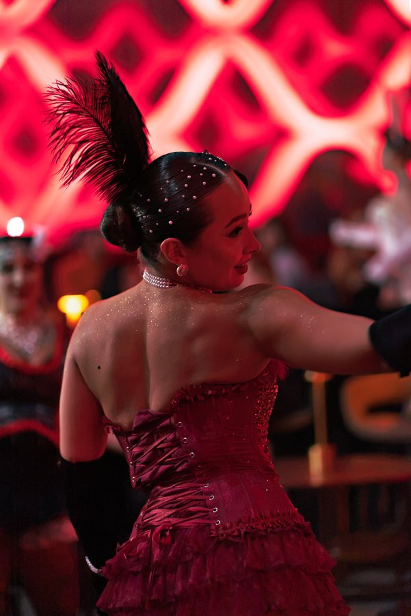 A dancer in a red sequinned costume seen from behind against the lattice wall.