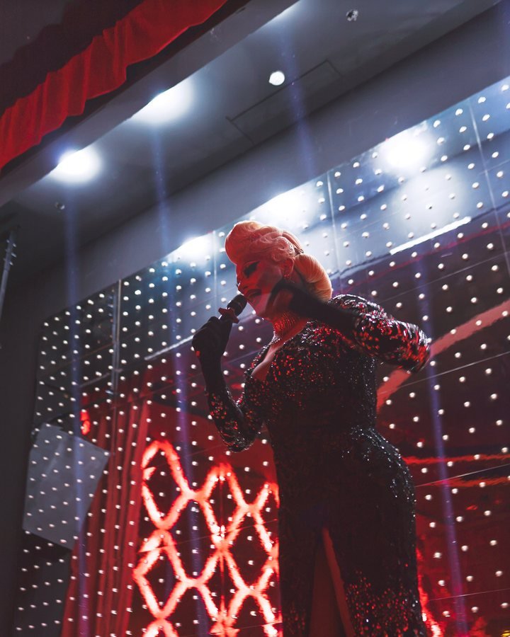 A cabaret singer in a feathered headpiece singing under the stage lights.