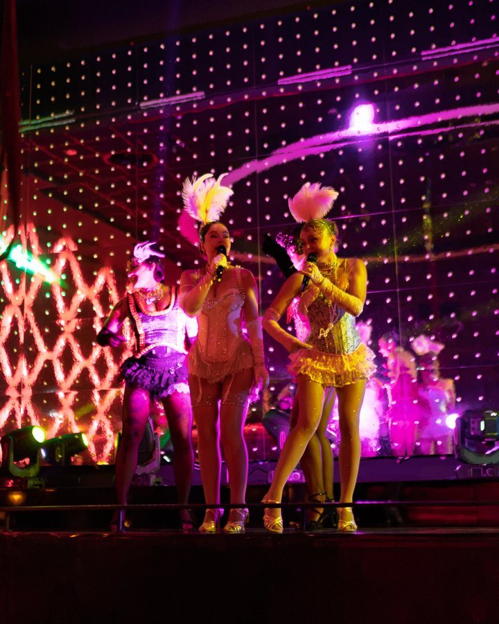 Showgirls in feathers and a gold costume performing on the neon-lit stage.