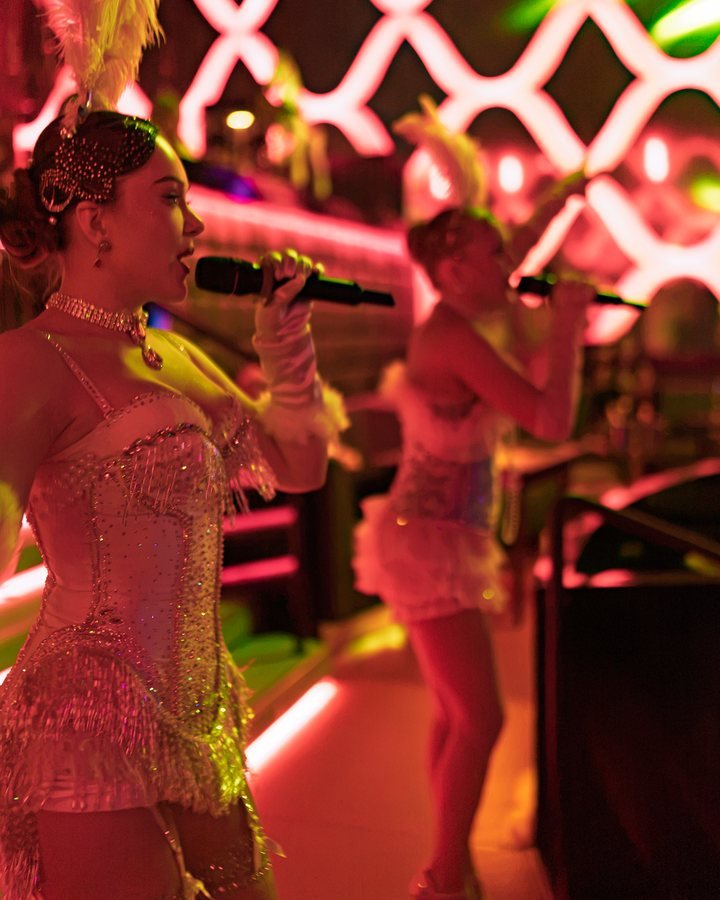 A showgirl singing into a microphone in a beaded costume and feathers.
