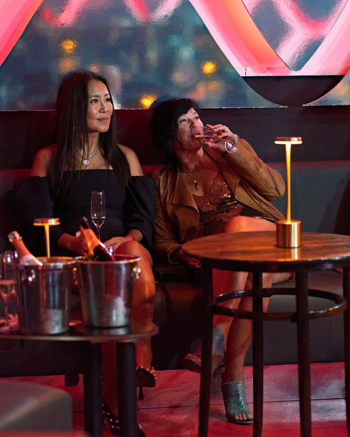 Two guests with champagne at a table beside the lattice wall.