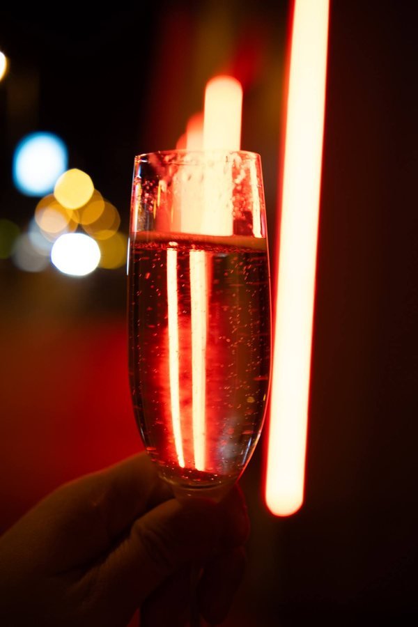 A glass of sparkling wine held up against red neon light.