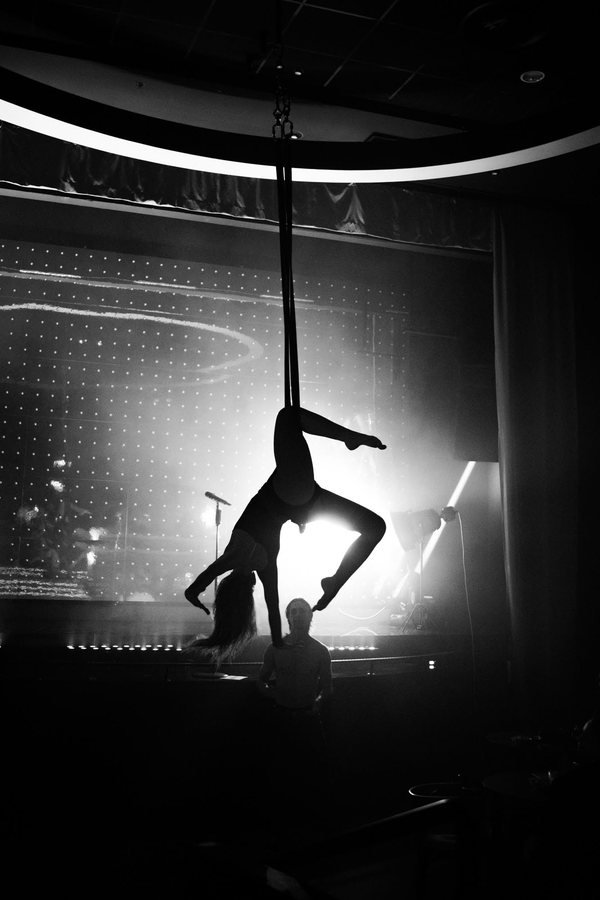 An aerialist suspended in silks above the stage, in black and white.