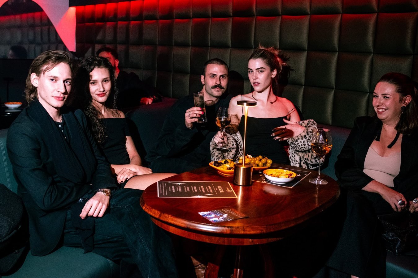 A group of guests posing in a velvet booth around a candlelit table.