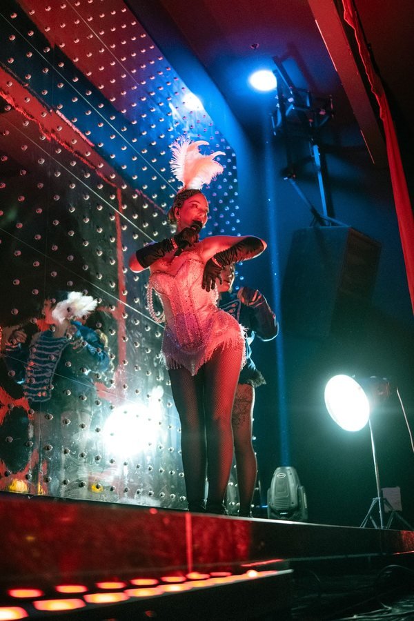 A showgirl in a white corset and feathers singing on the mirrored stage.