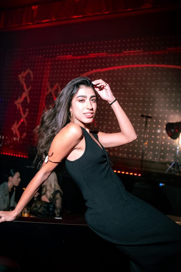 A guest in a black dress posing against the dotted light wall.