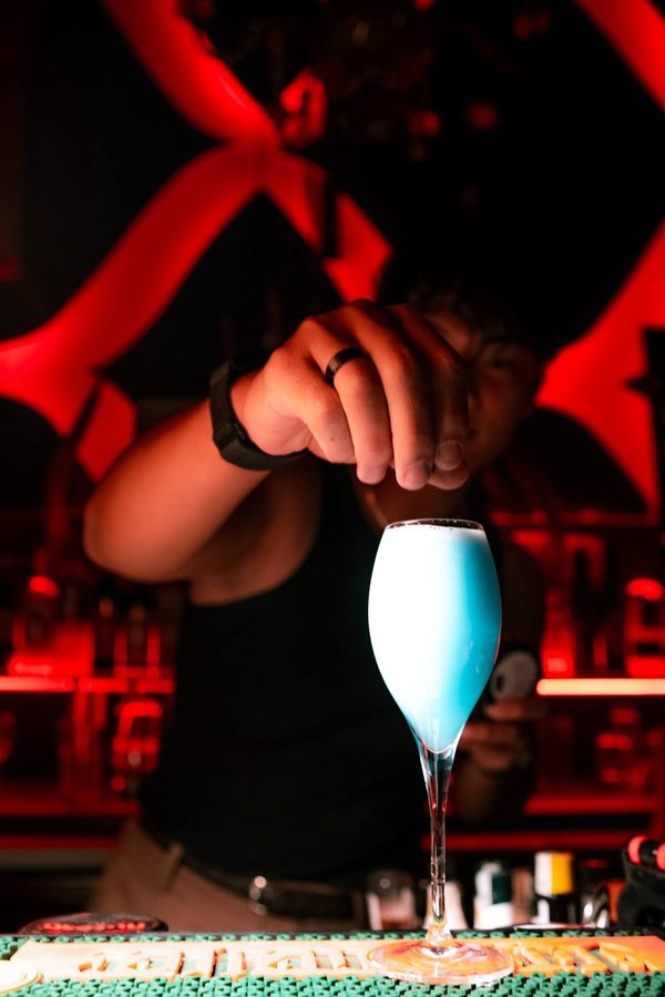 A bartender serving a bright blue cocktail at the bar.