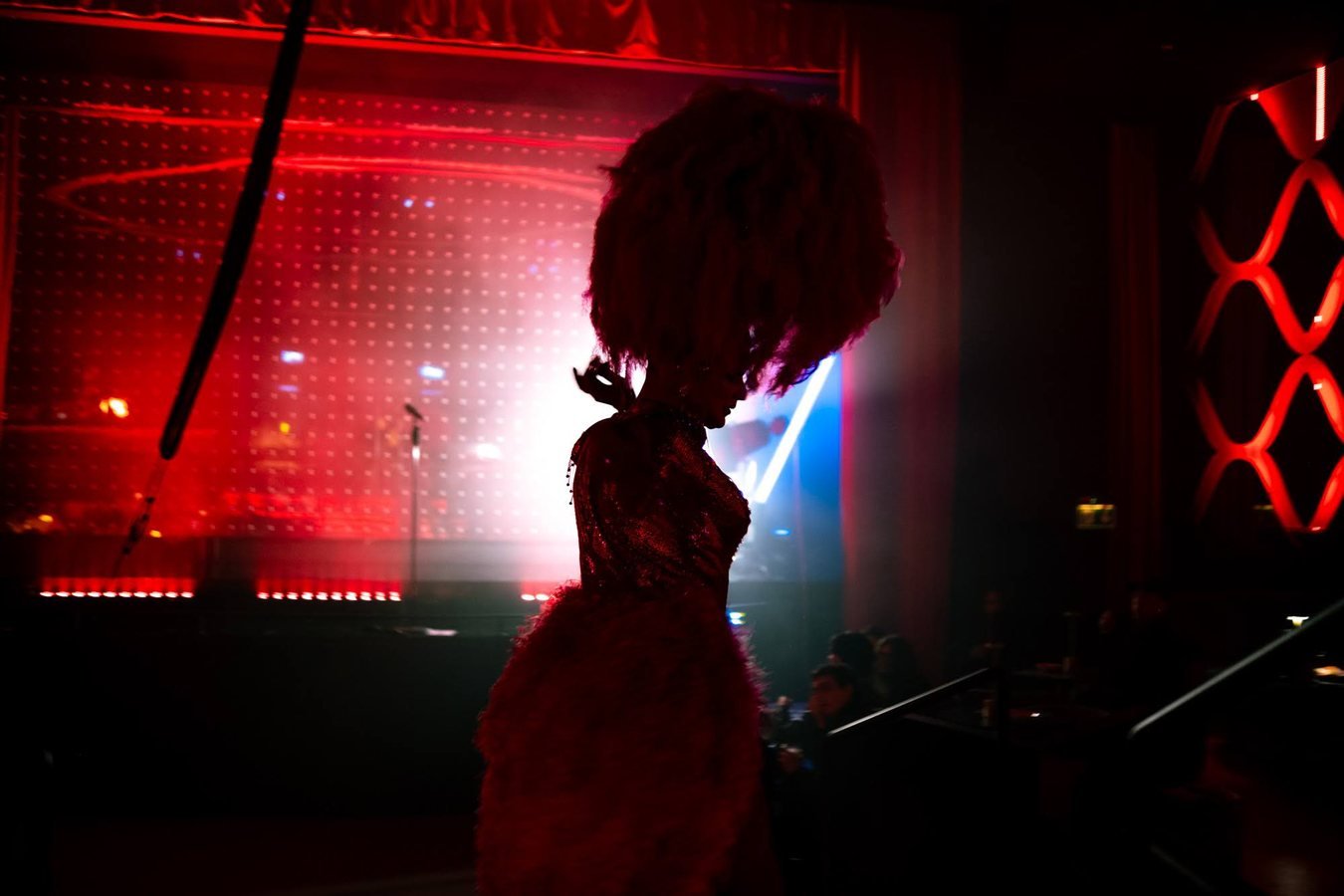 A showgirl in a towering red headdress, silhouetted against the red-lit stage.