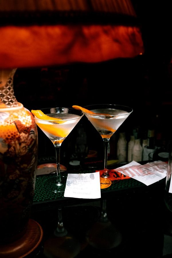 Two martinis with orange twists beside a lamp at the bar.
