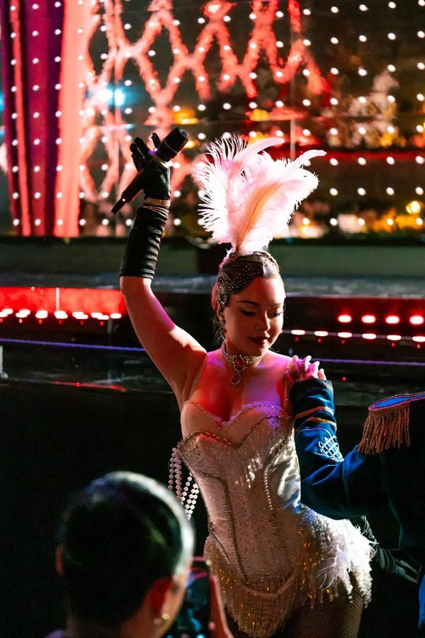 A showgirl with feathers and a raised microphone performing among the guests.