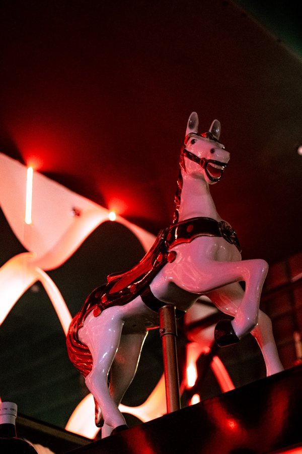 A white carousel horse lit in red beneath the lattice wall.