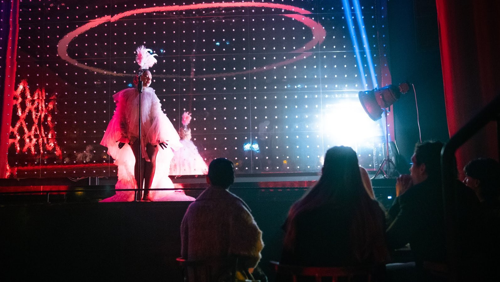 Guests watching a singer in a white tulle gown and feather headdress on stage.