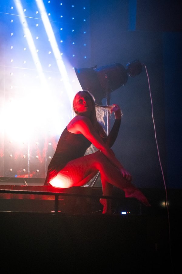 A performer sitting on the edge of the stage in red and blue light.