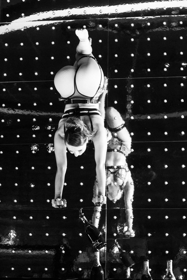 Two acrobats balancing in a handstand on the mirrored stage, in black and white.
