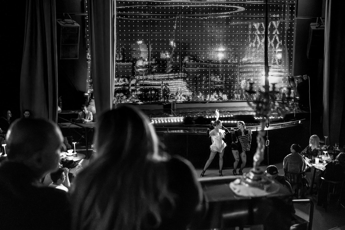 Guests watching two performers on stage from their tables, in black and white.