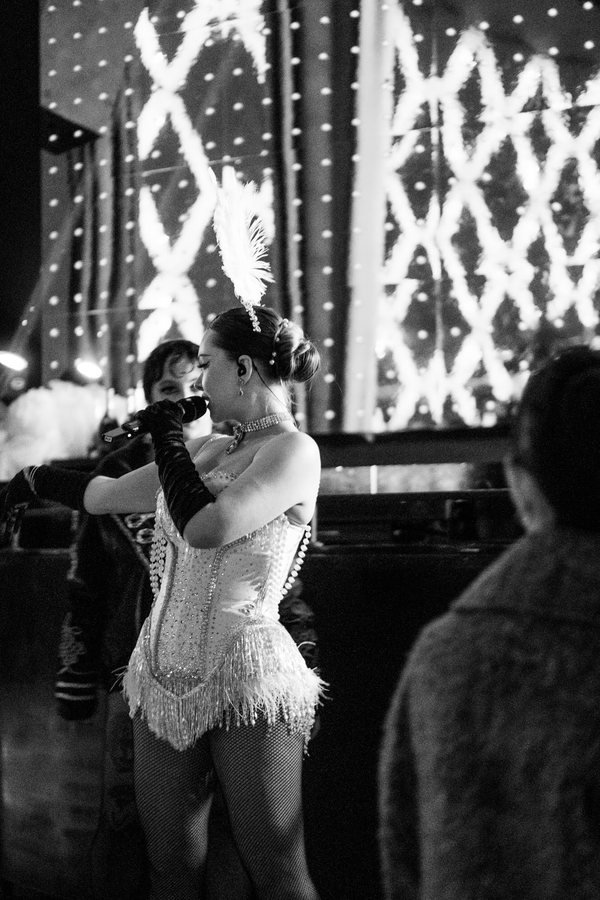 A showgirl in a white corset and feathers singing among the guests, in black and white.