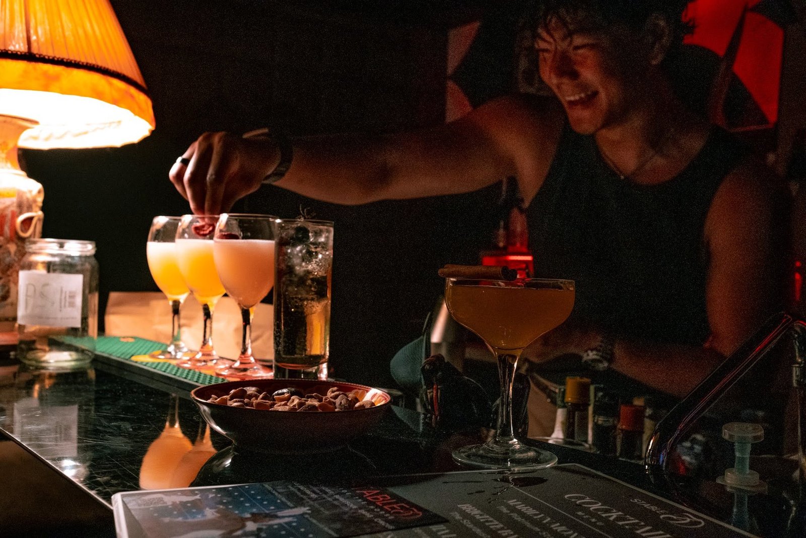 A smiling bartender garnishing a row of cocktails under a lamp at Stable 54.