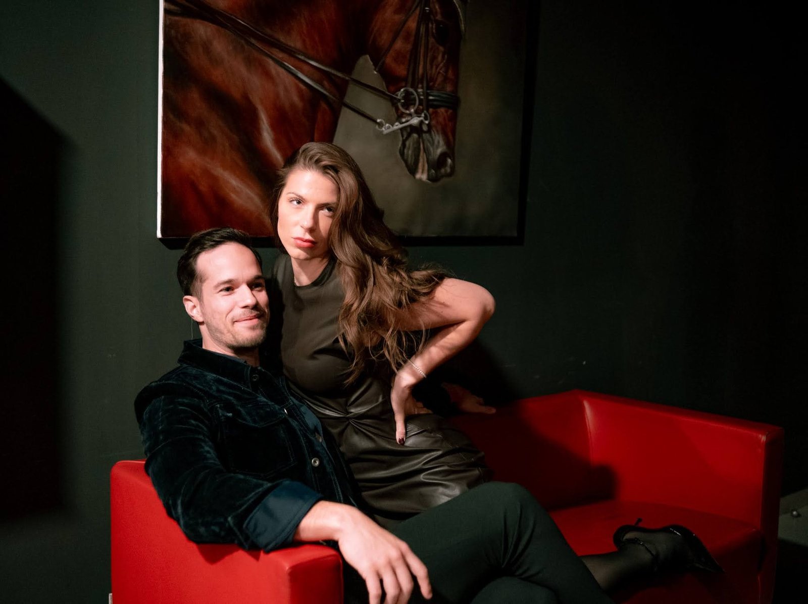 Two guests relaxing on a red sofa beneath a painting of a horse at Stable 54.